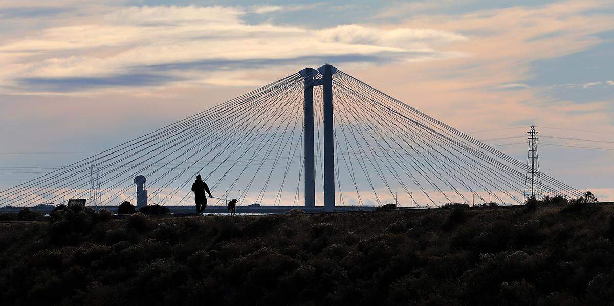 A dog walker is recently silhouetted against the cable bridge and an overcast sky while walking on the Franklin County shoreline pathway along the Columbia River in Pasco. The Tri-Cities can look forward to a rainy, breezy week with the possibility of dusting of snow on Rattlesnake Mountain, according to the National Weather Service forecast.