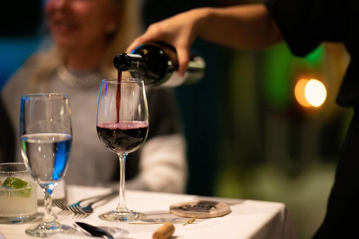 A waitress pours a glass of wine for guests at a restaurant.