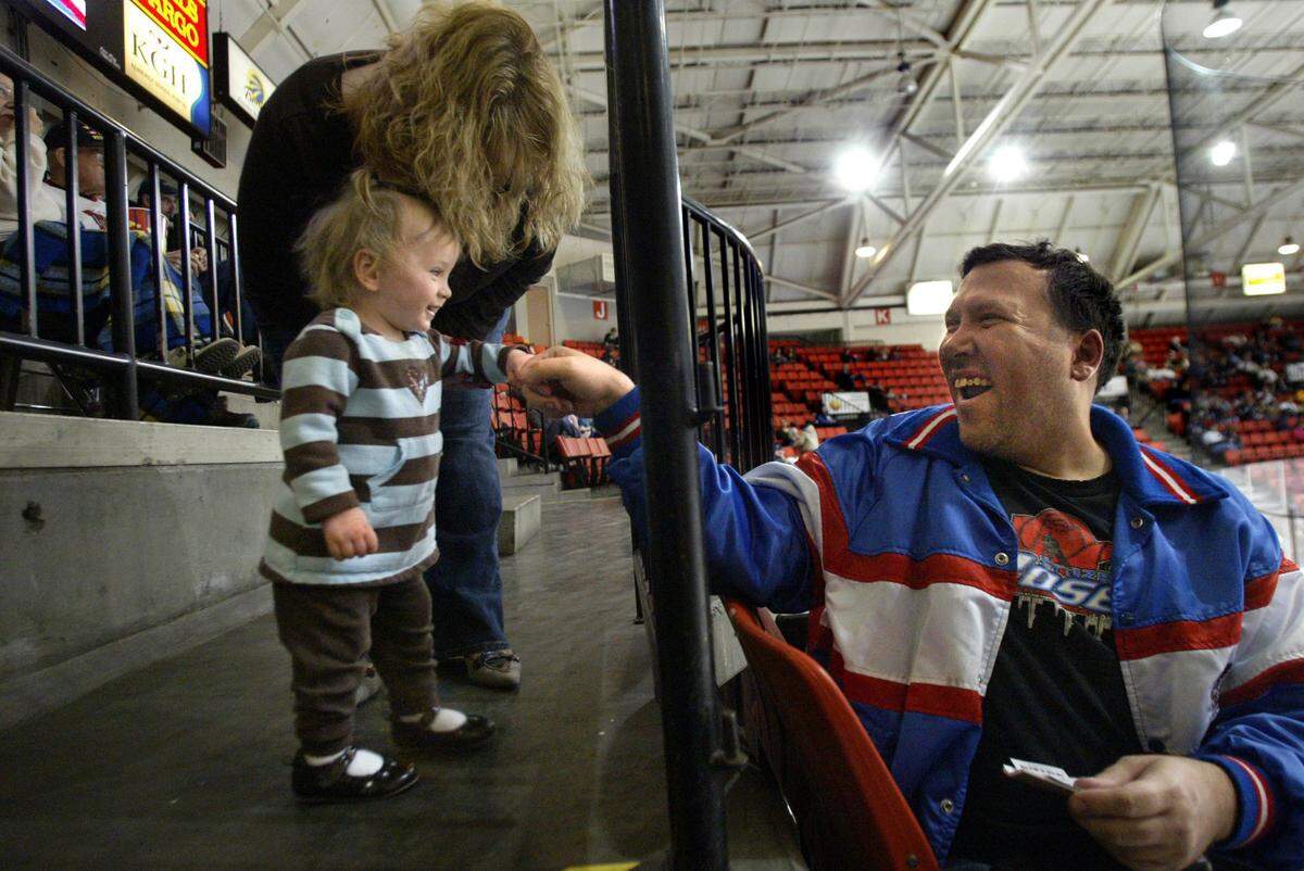 Young hockey fan Madison Moffett, 14-months, trades “knucks” and smiles with “Woo-Hoo” Jimmy Butcher of Kennewick during a Tri-City Americans hockey game 2010. Bumping “knucks” is Butcher’s ritual of celebrating Americans’ goals.