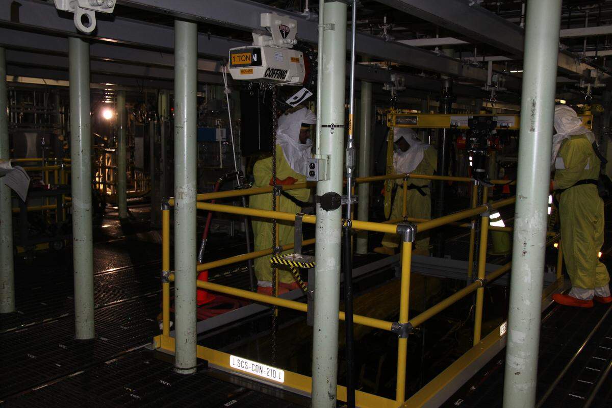 Workers in protective gear inside the K West Reactor Basin at Hanford start the first transfer of radioactive sludge from the basin into containers for shipment and storage at T Plant in central Hanford.