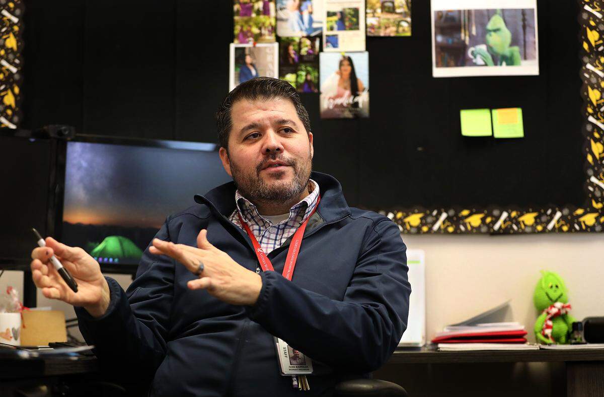 Ivan Barraza, a migrant graduation specialist, sits in his shared office discussing his role with students at Pasco High School.