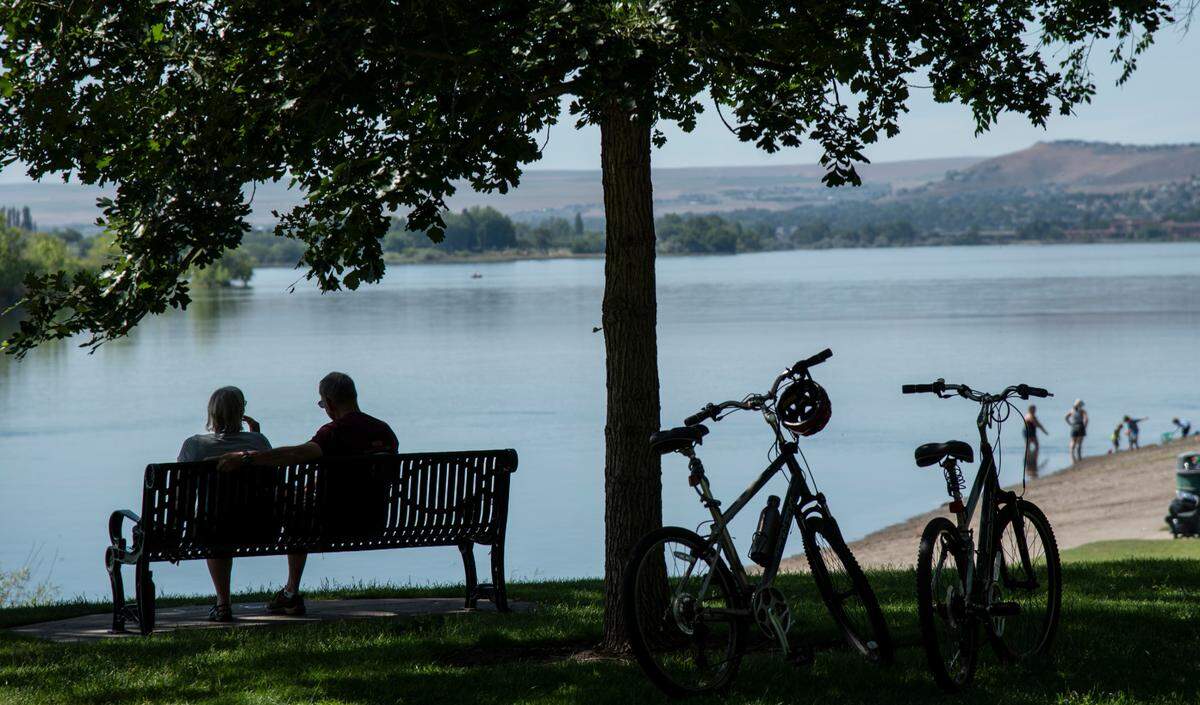 Bikers take a break on a bench in Leslie Groves park in Richland during the heat wave this week.