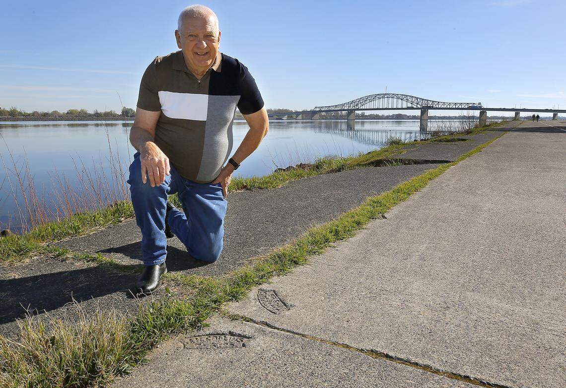 Local amateur historian Bill Glenn kneels near stampings from 1926 in adjoining sections of the century-old concrete highway in Kennewick's Columbia Park.