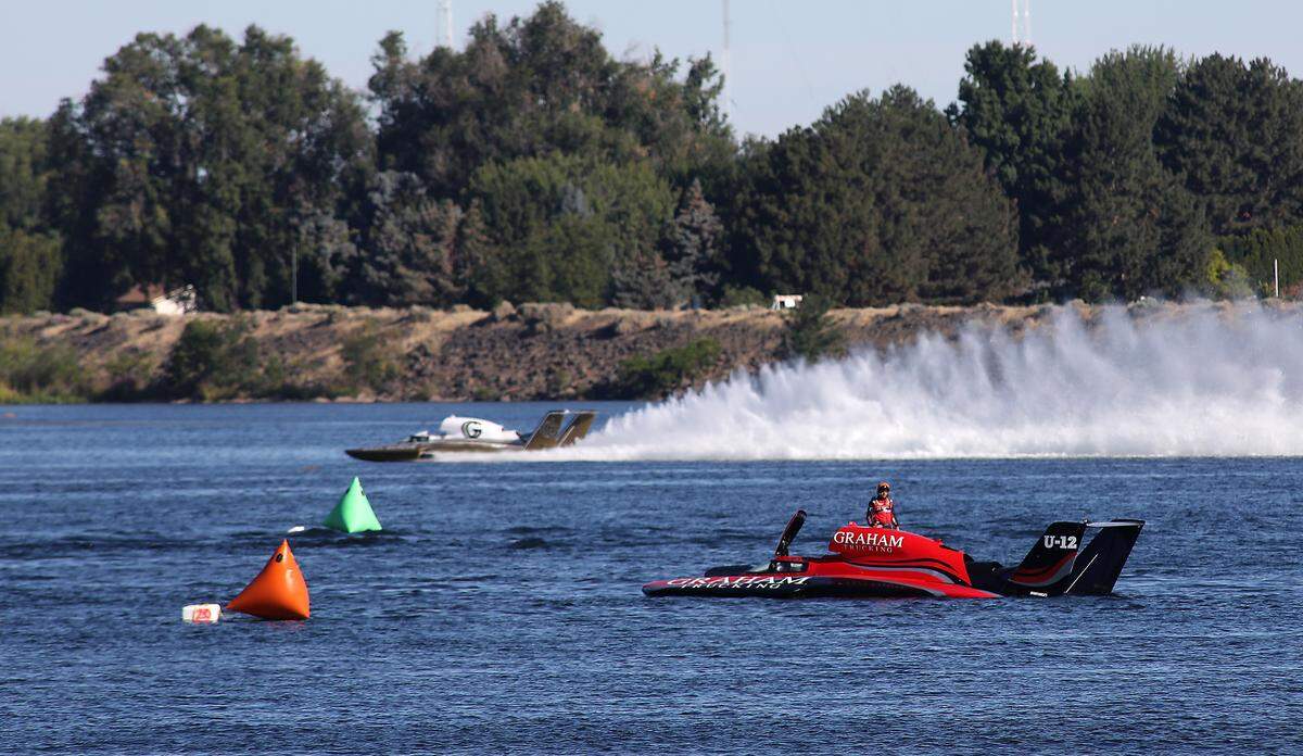 Jeff Bernard, driver of the U-12 Graham Trucking unlimited hydroplane, stands on the deck after a mechanical failure during Sunday morning testing session on the Columbia River in Kennewick. Andrew Tate in the U-91 Goodman Real Estate hydroplane goes past him in the background.