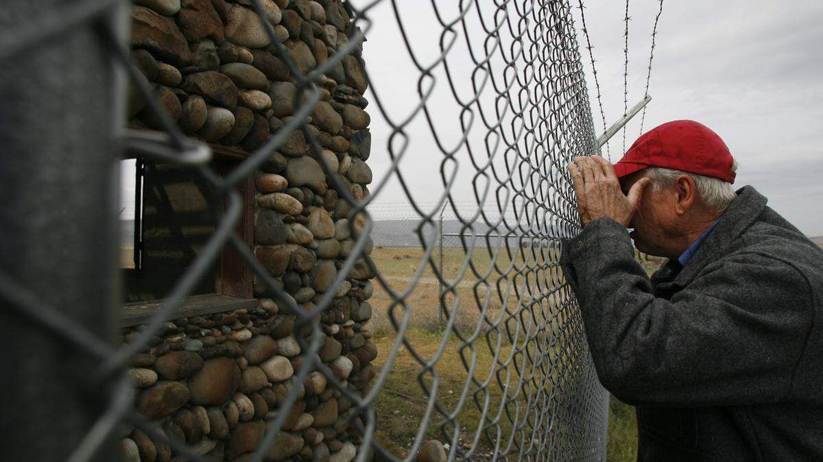 Ludwig Bruggemann peeks through a fence at the Bruggemann Warehouse, part of the ranch where his family lived before being evicted to make way for the Hanford nuclear reservation during World War II. The warehouse has been named a 2018 Most Endangered Place by the Washington Trust for Historic Preservation.