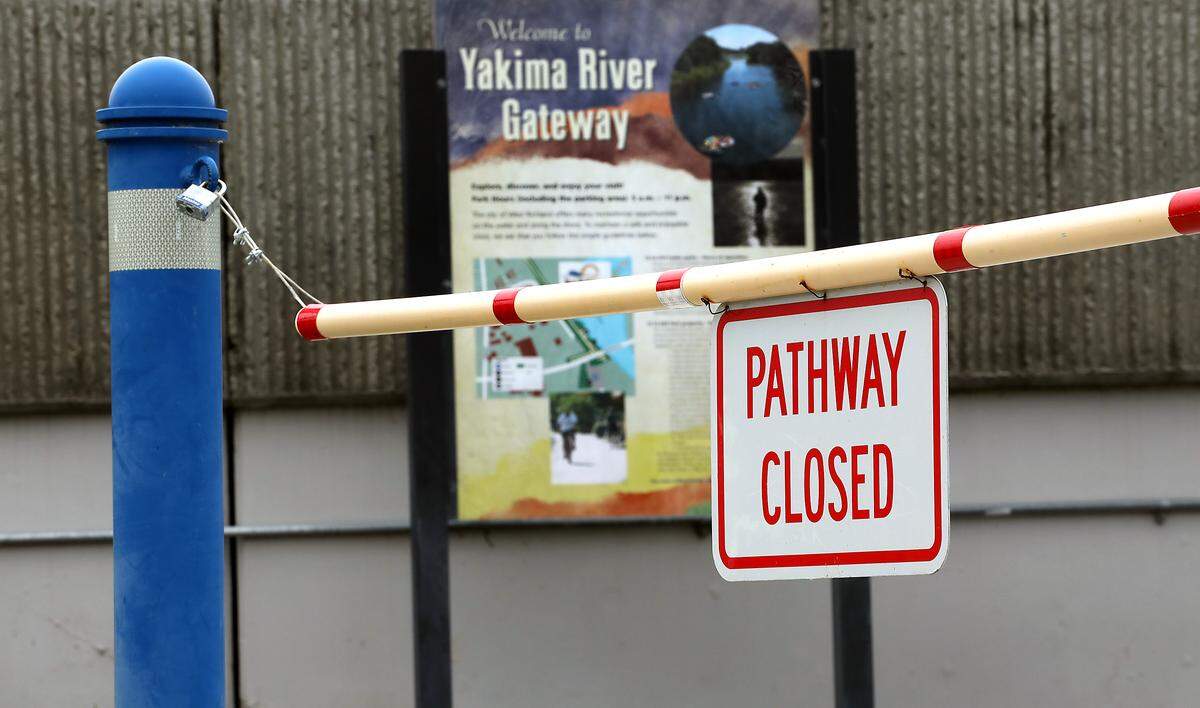Pulbic works employees places the "Pathway Closed" sign and barricade Tuesday morning along the Yakima River shoreline at West Richland's Yakima Gateway Park. 