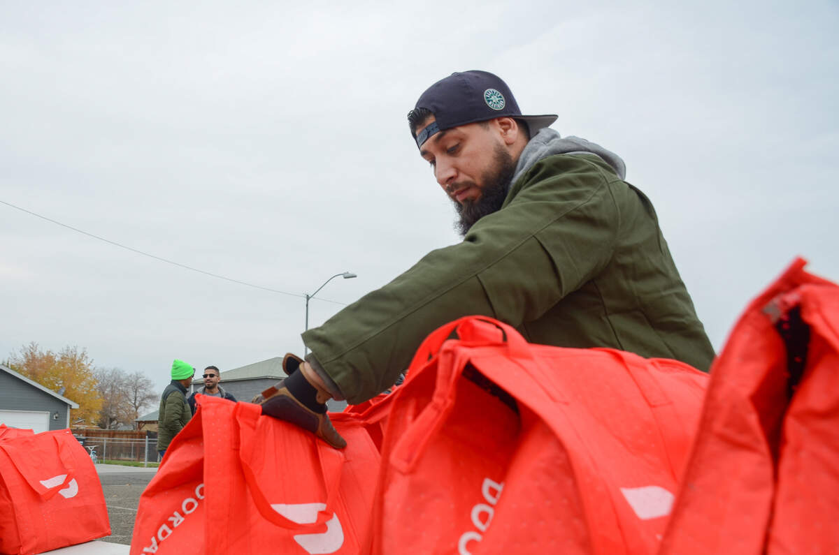 Volunteer Abraham Arousa, 33, of Kennewick, organizes DoorDash bags filled with turkeys and hams Saturday at a Thanksgiving meal distribution event held at Morning Star Baptist Church in Pasco, Wash.