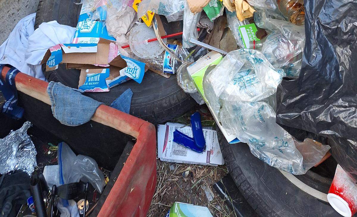A broken campfire lighter can be seen on top of a box of Naloxone in a pile of debris hidden by a massive pile of dumped tires in Kennewick.