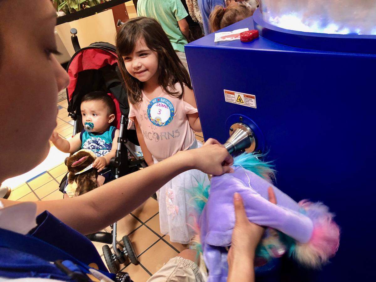 Selena Torres, 3, waits for her unicorn to be filled Thursday by Tatiana Collado at the Build-A-Bear Workshop at Columbia Center mall in Kennewick. Selena is the daughter of Diana Torres of Pasco.