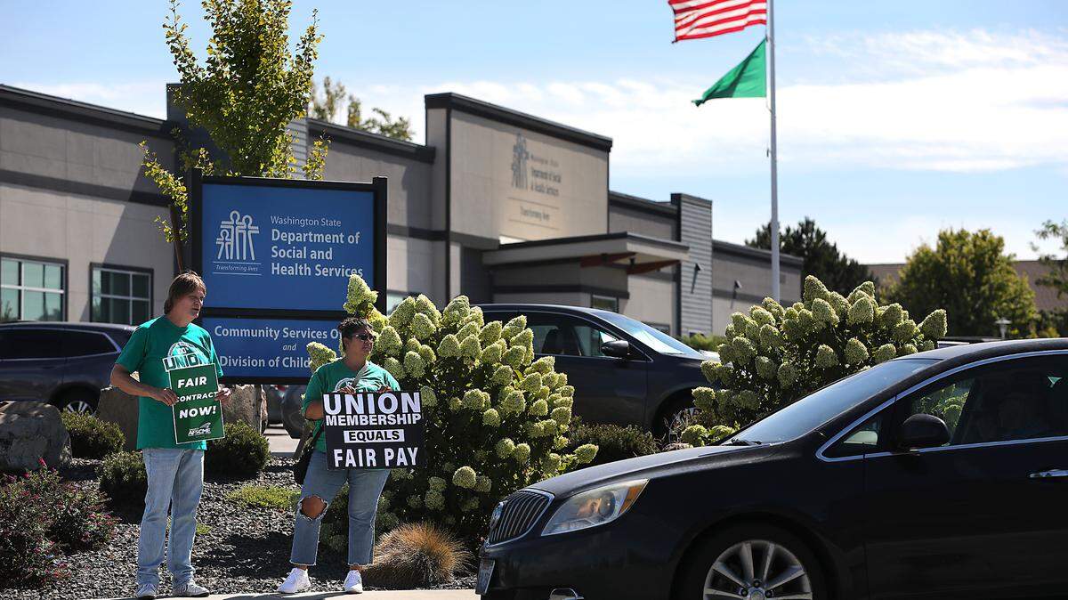 Tri-Cities union members Doug D’Hondt, left, a Department of Ecology employee, and Abrisa Rodriguez, a Department of Social & Health Services employee, hold signs in front of the DSHS office Tuesday during a statewide walkout by members of the Washington Federation of State Employees. 