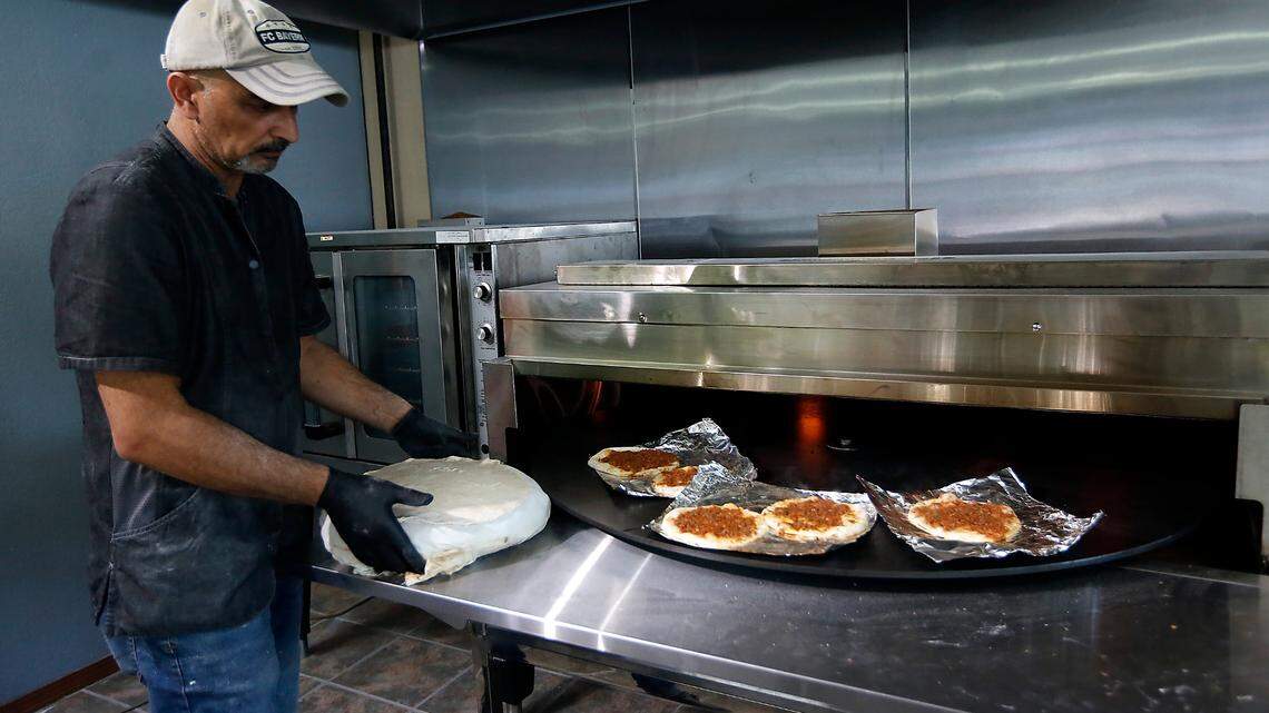 Al-Hayyawi Adnan Hussein, owner of Somer Bakery, prepares to bake flat bread as Lahm Bi Ajeen spins through the oven at his recently opened business. The classic Iraqi dish is described as an Iraqi pizza.