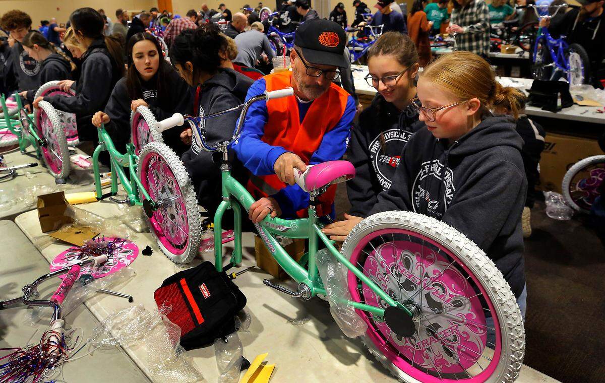 Jim Millbauer, Bikes for Tikes board member, mentors Tri-Tech Skills Center students Emily Little, left, and Sadie Stacy as they build their first ever bicycle during Thursday’s 2024 Bikes for Tikes build day.