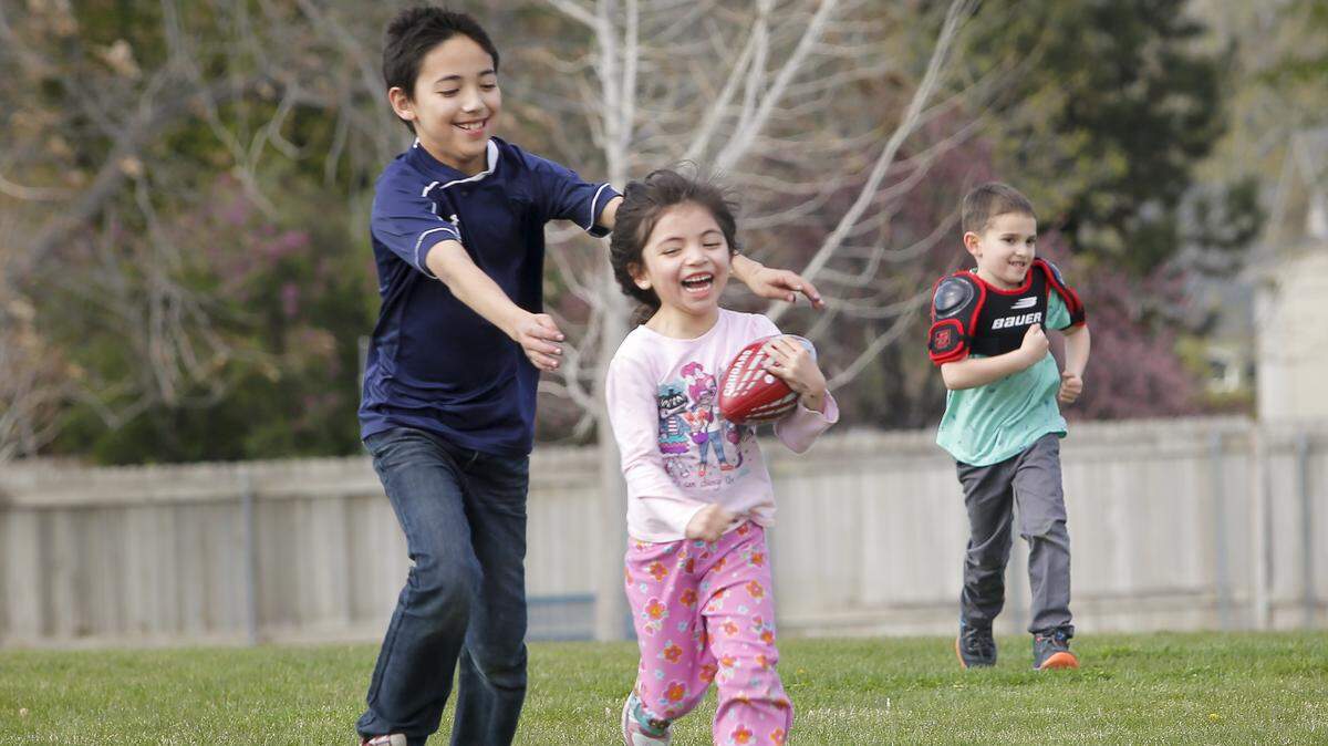 Rudy Angulo, 10, left, and Brayden Buxbaum, 4, right, chase after Vida Angulo, 5, as she runs with a football on Saturday at Highlands Grange Park in Kennewick.  Siblings Rudy Angulo and Vida Angulo were accompanied by Brayden Buxbaum's mother, Maria Buxbaum, of Kennewick.