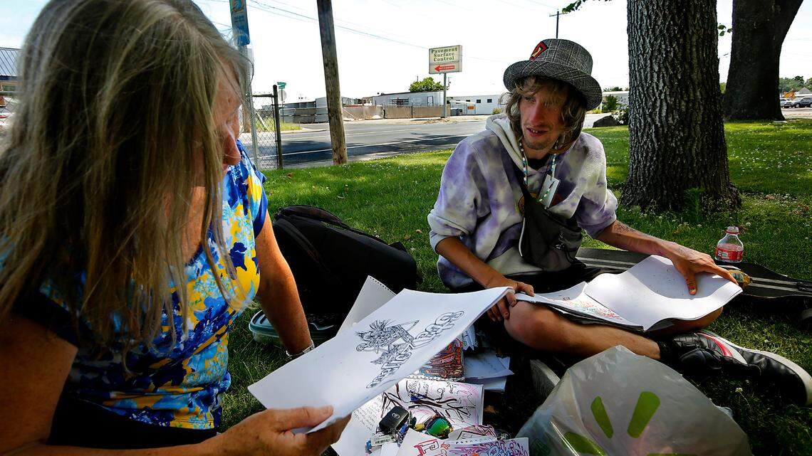 Community volunteer Cindy Fish sits with Steve-O Wold, 29, in Kennewick’s Fruitland Park as he explains his meaning of the drawings he spends hours creating. She has helped Wold, who has lived on the streets since he was 16 and is in the process of applying for housing. 