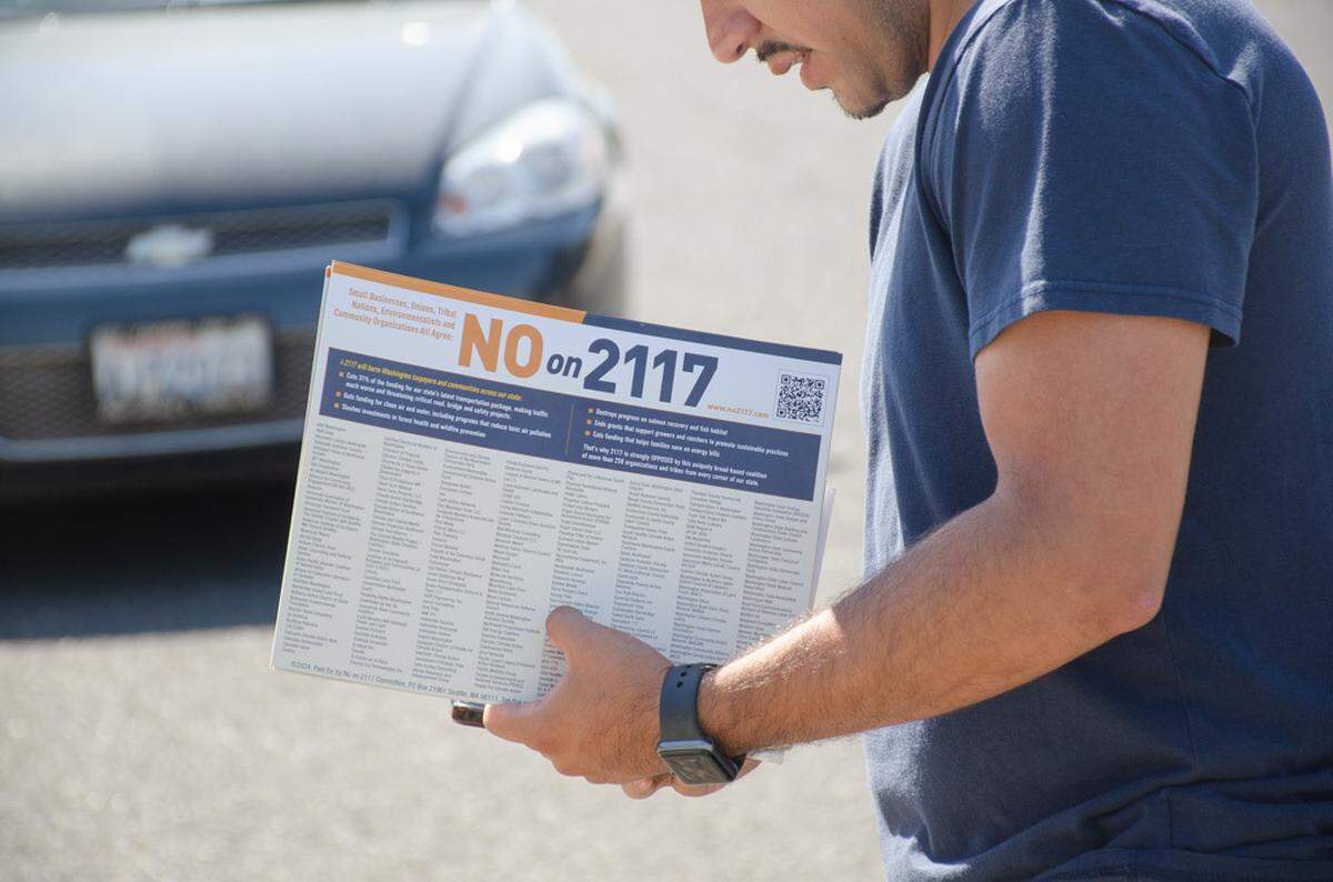 Mark Figueroa, Washington state coordinator with Poder Latinx, checks maps Tuesday, Sept. 3, in a West Valley neighborhood during a nationwide voter registration and mobilization effort. He holds in his hands campaign materials opposing Initiative 2117, which would repeal sections of Washington’s Climate Commitment Act if passed Nov. 5.