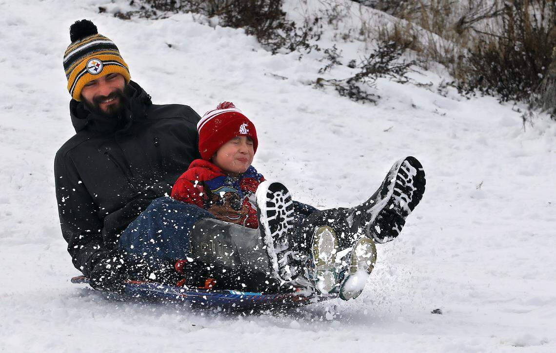 Jonathan Agreda of Kennewick and his five-year-old son, Xavier, are sprayed in the face with snow while sledding on a vacant land on South Vancouver Street near West 7th Avenue during a snow day from school in Kennewick. 