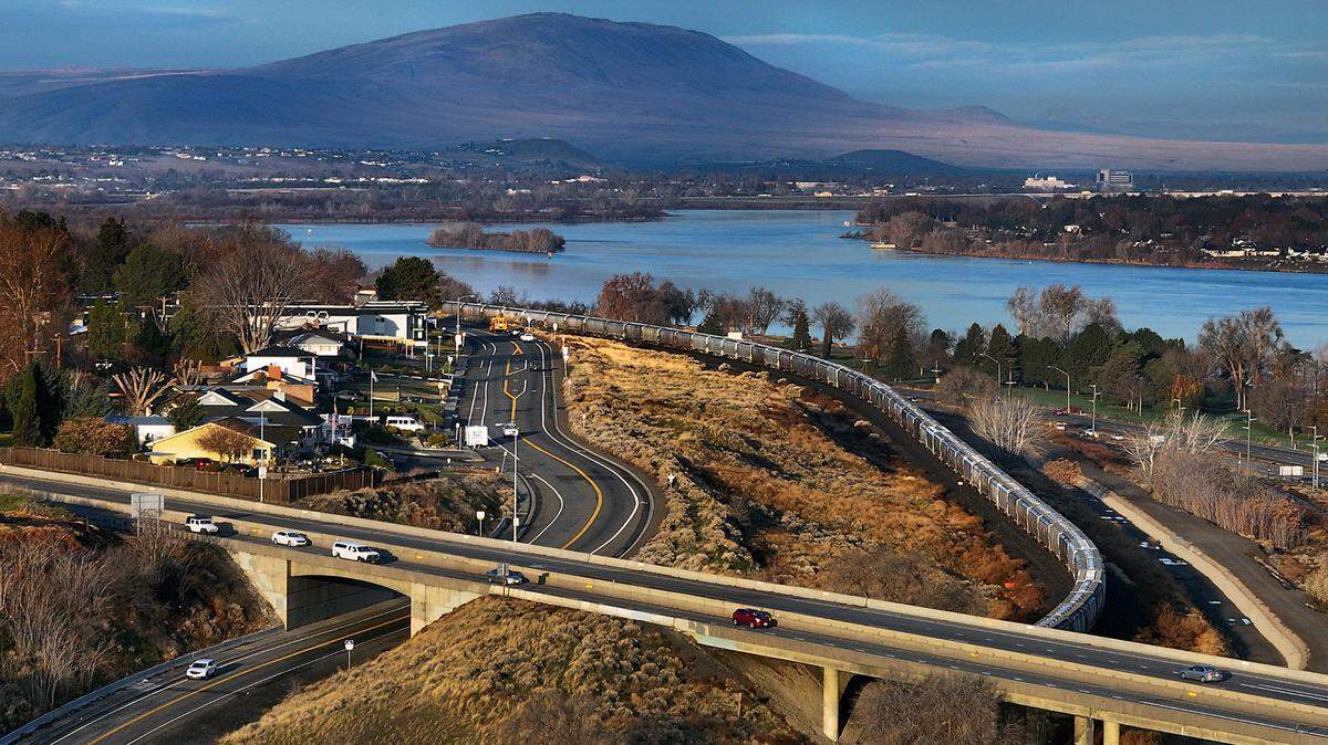 Highway 395 overpass crosses West Canal Drive in Kennewick with railroad tracks, Columbia River and Rattlesnake Mountain in the background.