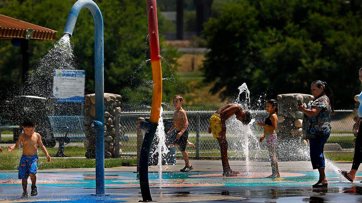 Kids and adults chill out at the splash pad at the Playground of Dreams on a hot and sunny summer afternoon at Kennewick’s Columbia Park. The forecast calls for temperatures to reach triple digits through the weekend before cooling off into the 90s next week.