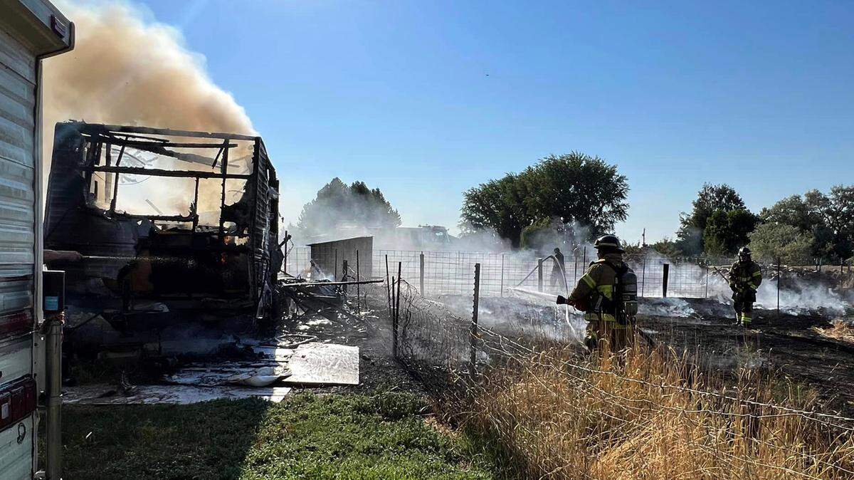 Firefighters work to extinguish a travel trailer and burning grass Sunday afternoon in Finley. A dog was trapped inside and died.