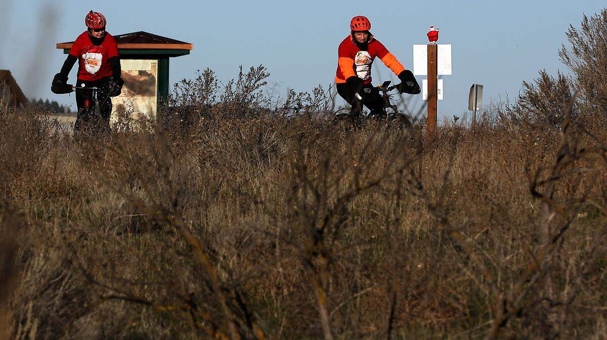 James McCullough of Kennewick pedals his mountain bike towards a conspicuously “hidden” Santa decoration at the start of the 2023 Chamnarama Santa Scavenger Hunt held at the Chamna Natural Preserve in Richland. His riding partner, Lamar Linde of Kennewick, follows him on the trail out of the preserve’s parking area.