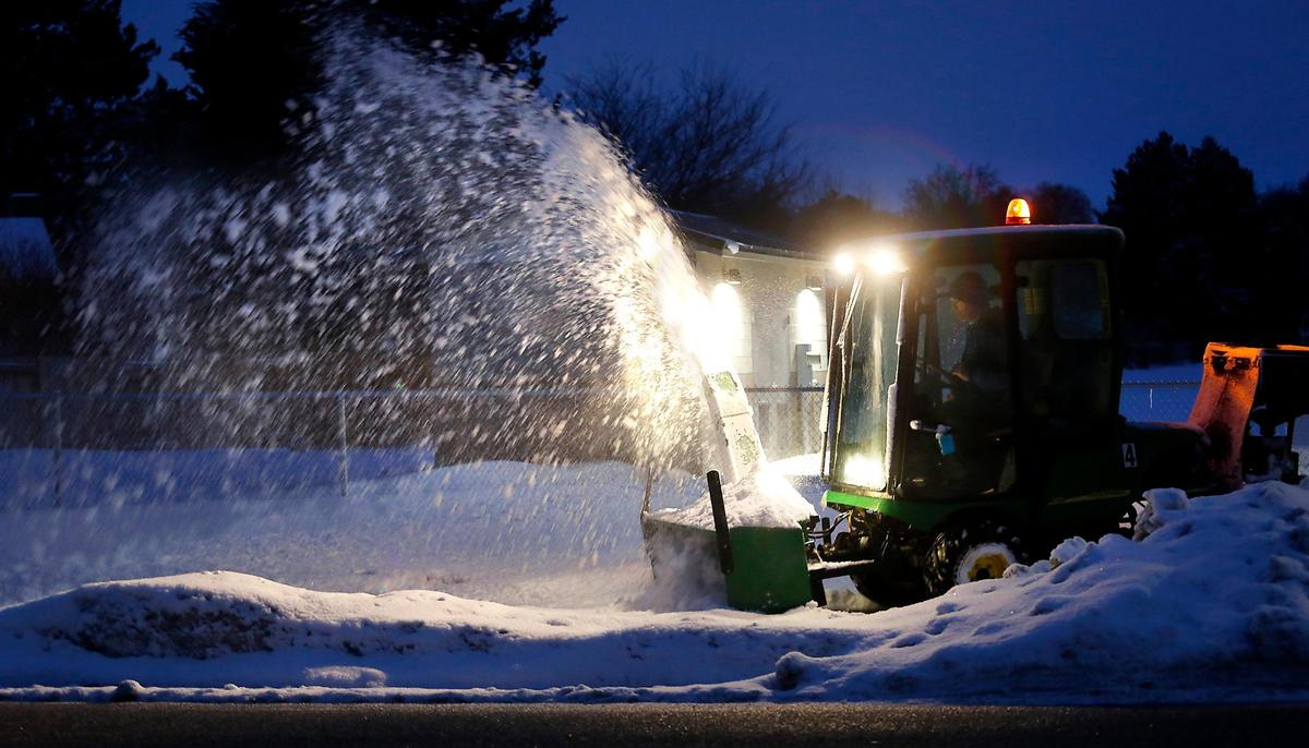 Snow flies from the chute of a tractor-mounted snowblower before dawn Monday morning as a Kennewick School District clears sidewalks near South Garfield Street near Park Middle School. Many area school districts have delayed the start of classes because of the winter weather conditions.