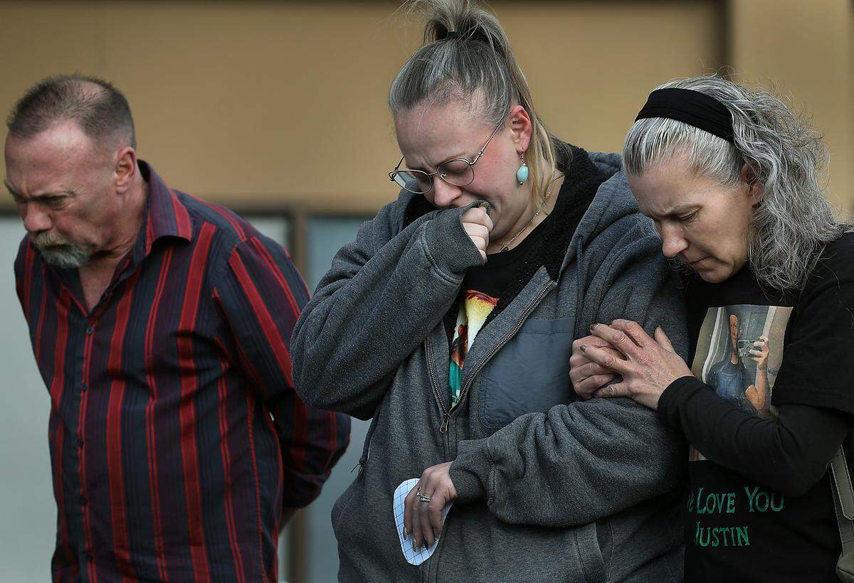 Krista Schaaf, middle, is comforted by friend Vikki Shaw during a brief outdoor memorial service for Schaaf’s brother Justin Krumbah. Mark Hill, far left, was also shot and wounded that day.