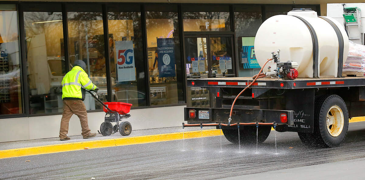 Giovanni Rodriguez, an employee of Columbia Property Management, uses a broadcast spreader Thursday morning to distribute ice melt granules on the sidewalk at the Columbia Square while his co-worker sprays liquid de-icer in the parking lot of the retail mall in Kennewick . A series of winter storms is expected to deliver several layers of snow across the Pacific Northwest into early next week.