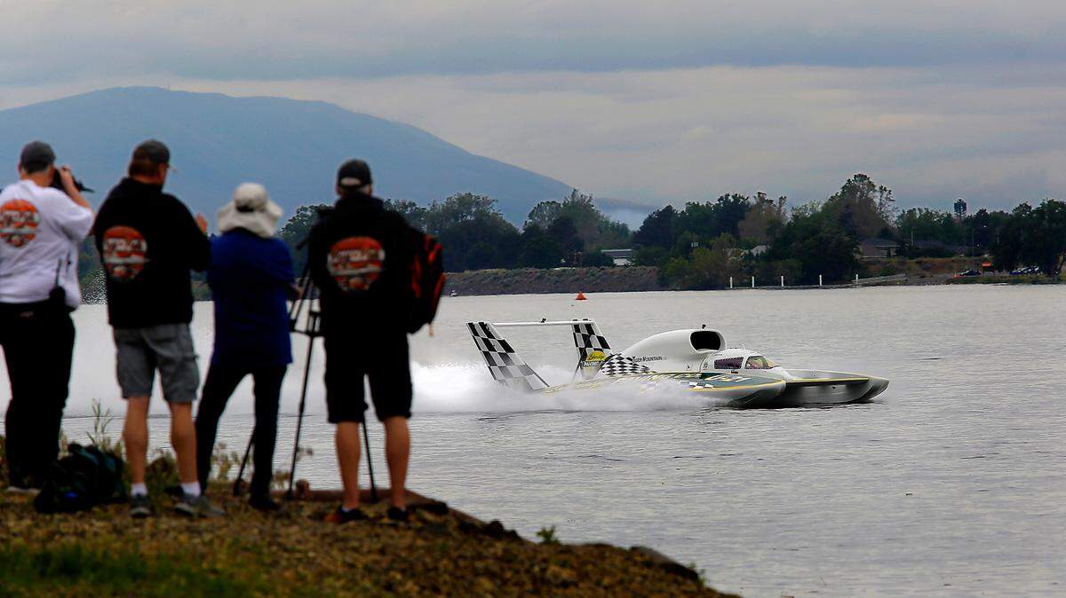 The U-21 Miss Lakeridge Paving unlimited hydroplane being driven by Brian Perkins zips past Kennewick shoreline and racing fans on the way back to the pits Friday following the first test run of the spring testing day on the Columbia River.