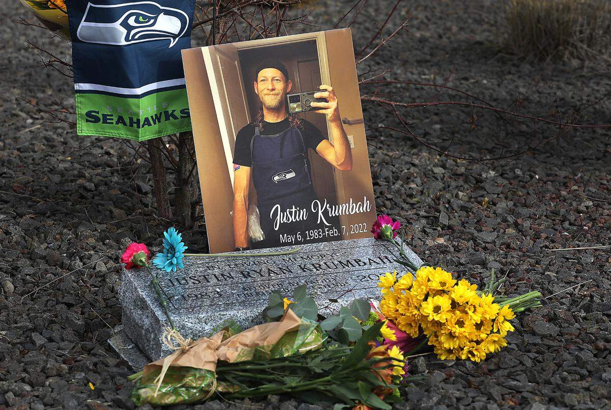 Flowers, a Seahawks flag and a poster decorate the memorial marker for Justin Krumbah outside the Fred Meyer store on Wellsian Way in Richland on the second anniversary of his shooting death. The Instacart worker, was killed and store employee Mark Hill was seriously injured during the crime on Feb. 7, 2022. Aaron C. Kelly, 41, is charged with first-degree murder and attempted first-degree murder.