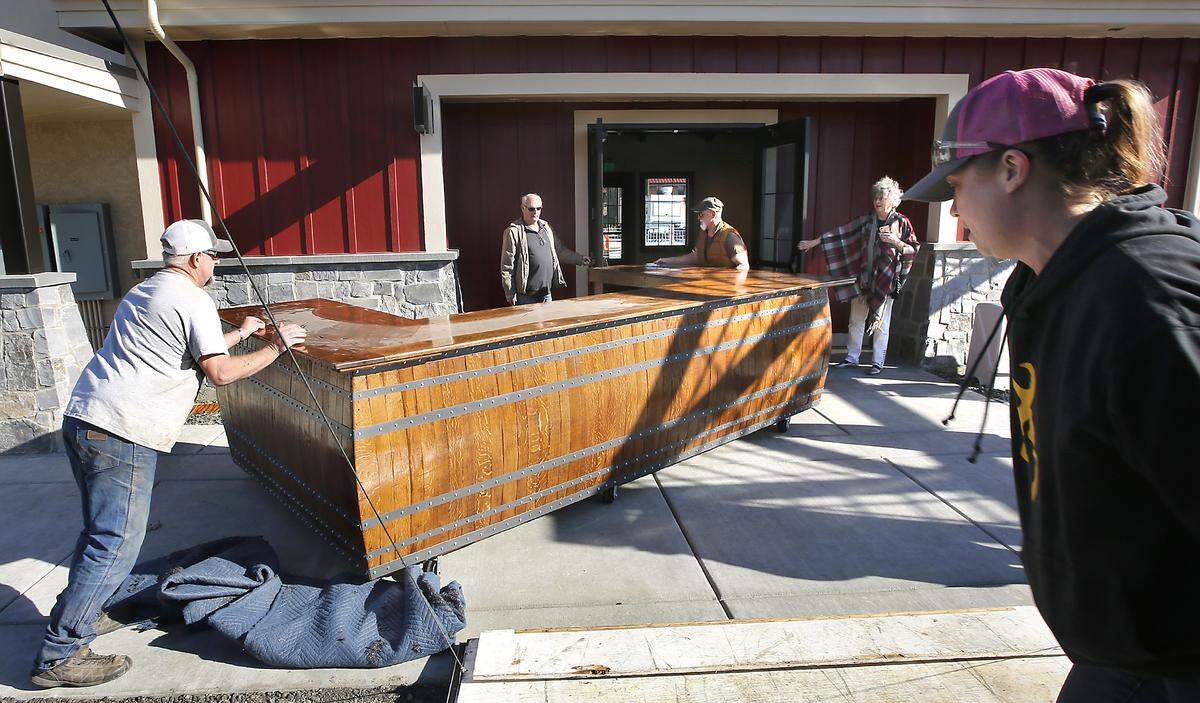 Shawn Harmon, left, and his father, Dan, maneuver a 12-foot wine bar built by The Rustic Barrel through the doors of the Gordon Estate Tasting Room at the Columbia Gardens Wine & Artisan Village on Columbia Drive in Kennewick. Jeff Gordon, center, and his wife, Vicki, hold the doors for the 400-pound rolling tasting bar. Watch a video at: tricityherald.com/videos