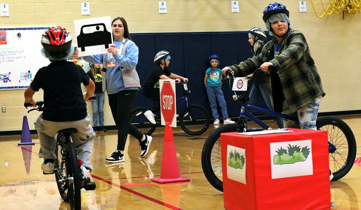 Jaid Lopez, PE teacher at Canyon View Elementary, holds up a sign representing a car on the road as fifth-grade students take part in the Let's Go bicycle education and safety program.