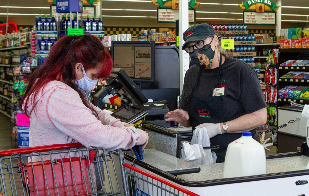A cashier at Red Apple Market in Kennewick helps customers ring up and bag groceries.