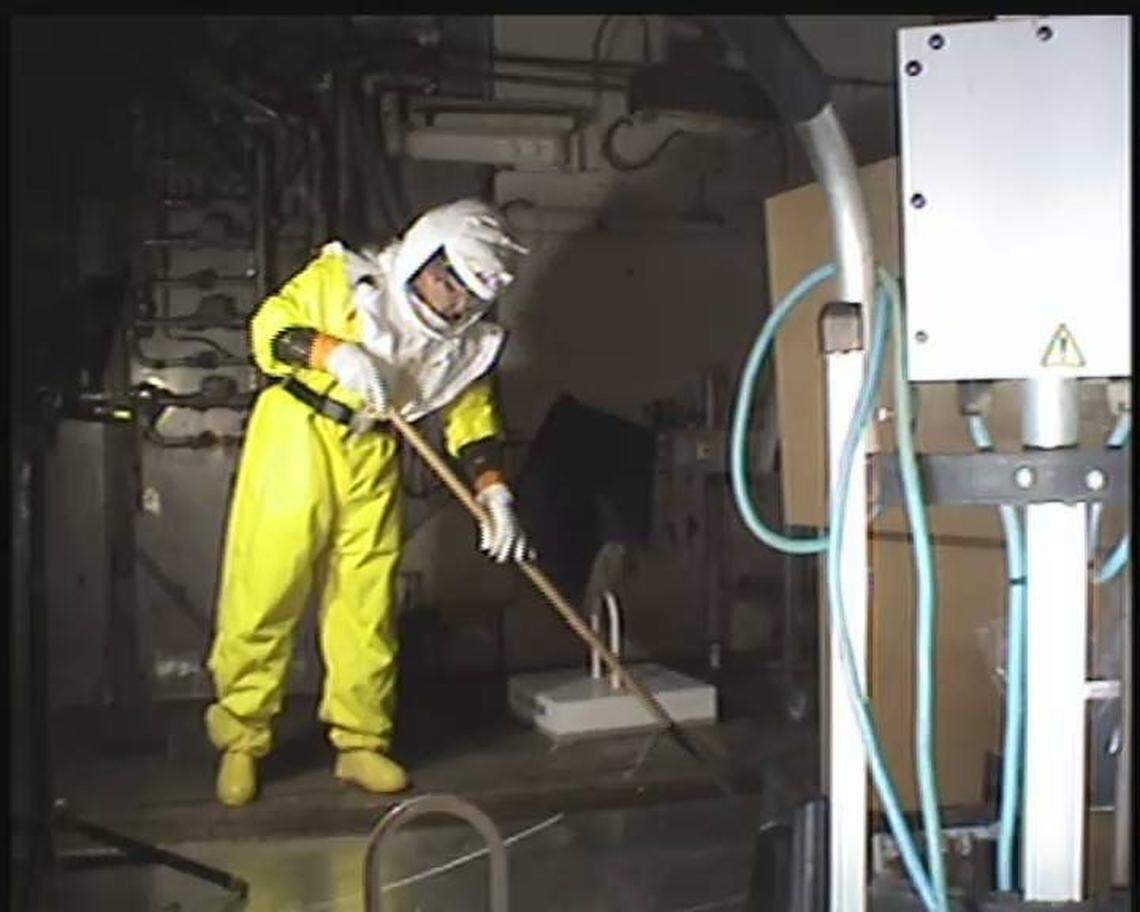 A Hanford worker in protective gear cleans out a floor drain trench in the 324 Building. Beneath the building is a spill of high level radioactive waste.