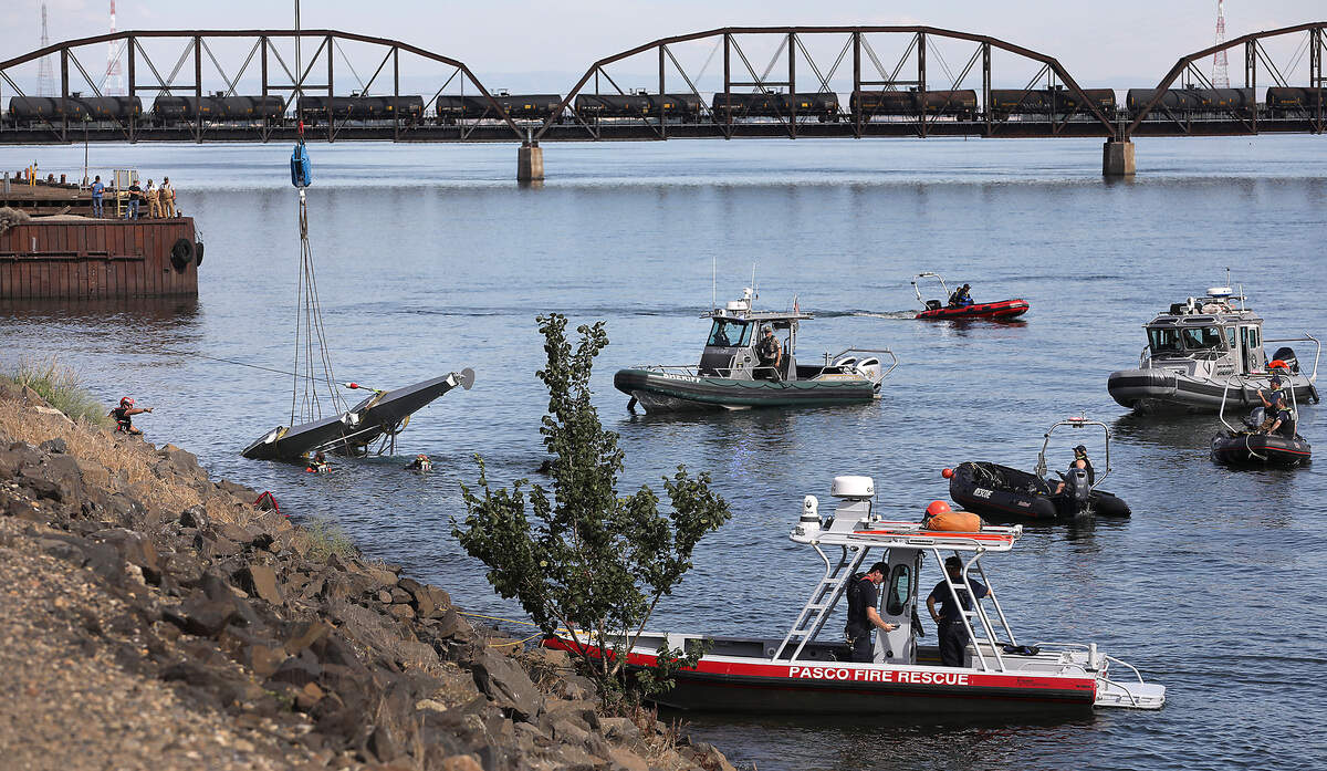 A flotilla of rescue boats surround the submerged floatplane that crashed into Columbia River Wednesday as a crane prepared to lift it from the water just below the cable bridge. Two men onboard were killed.