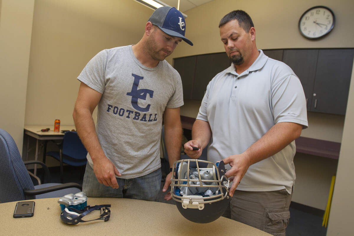Liberty Christian football coach Craig Lukins, left, and Jeff Boyus, president of the Kennewick Grid Kids Association, shows how the Cue sensor goes inside a football helmet. The Grid Kid football program is investing in the devices to monitor the number and severity of hits.
