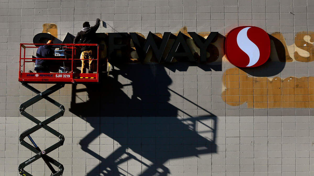 Workers on a scissor lift carefully paint around a new Safeway sign to cover the outlines of lettering at the former Albertsons grocery store on West Clearwater Avenue in Kennewick.