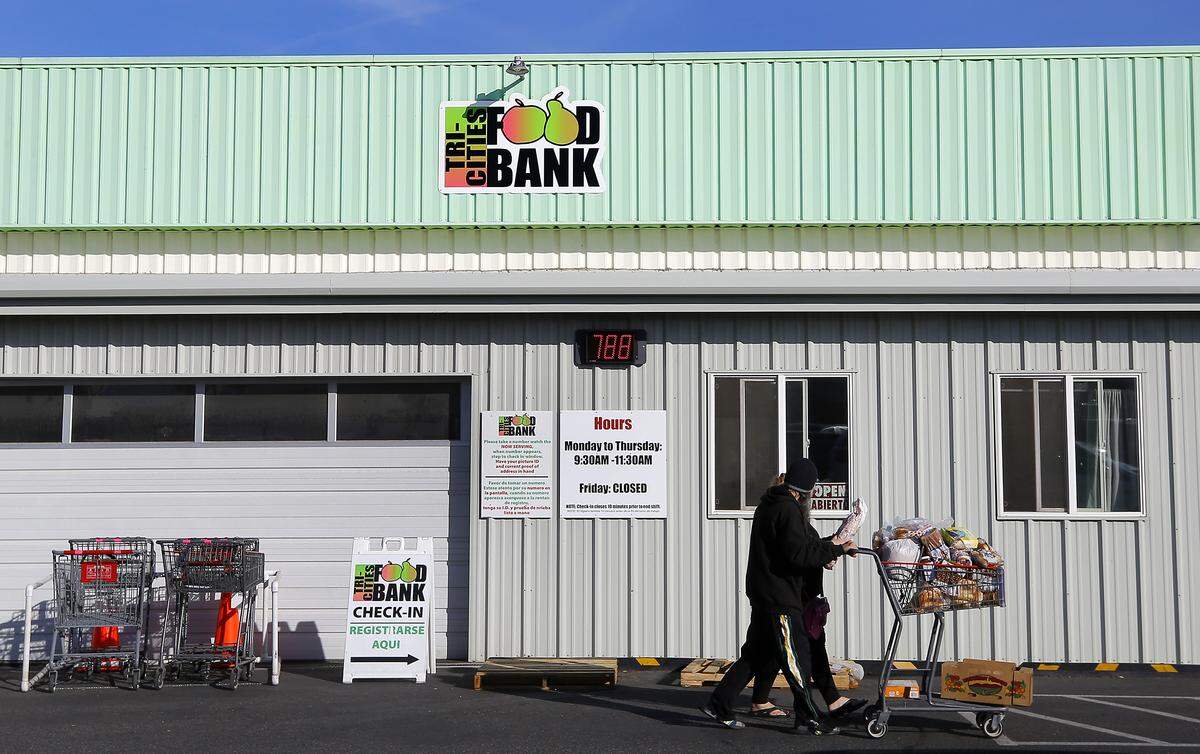 Clients leave with a grocery cart is filled with food recently at the Kennewick branch of the Tri-Cities Food Bank. Volunteers work from a list to fill carts depending on the family size and any dietary requests.