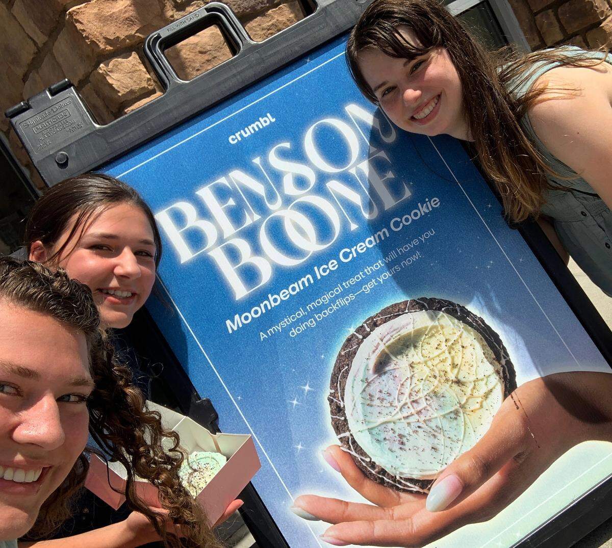 Valerie and Olivia Thomas and Kate Hulick pose with Crumbl’s poster for its Benson Boone-inspired cookie.