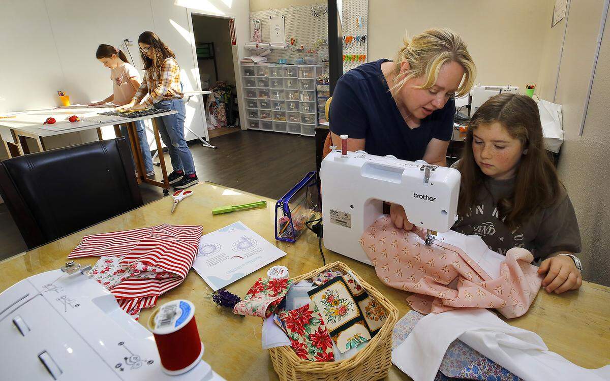 Jessica Beck, owner of Jessica's Sewing School, helps student Sofia Curran, 9, with a project during a recent class at the Kennewick business. Students Maisie Nolte, 10, left, and Lucca Taranto, 15, work at cutting fabric for the next step of their projects.