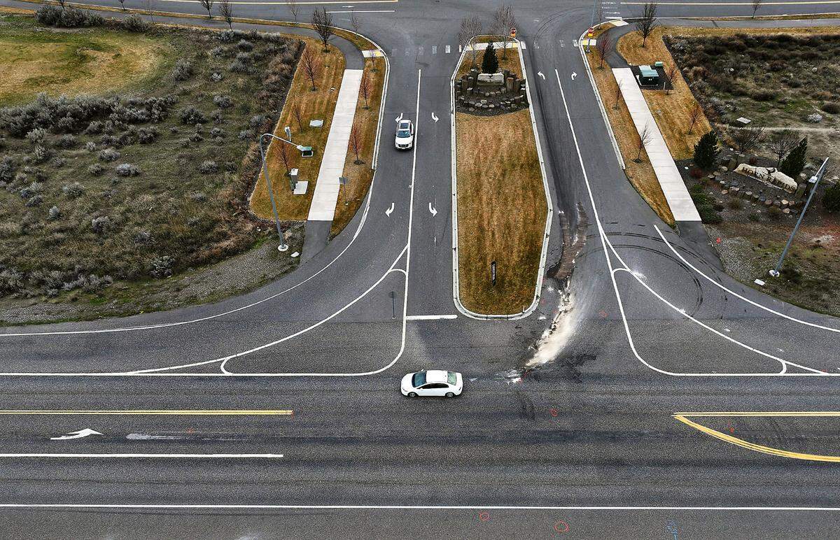 Motorists drive past investigative paint markings, engine fluid stains and debris from the March 1 collision at the intersection of Highway 240 and Village Parkway near the Horn Rapids housing development in Richland. 