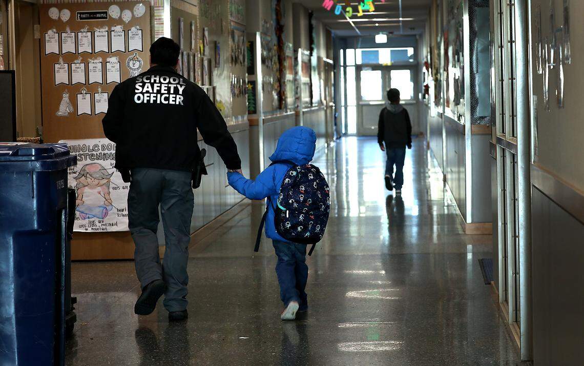 School safety officer Roman Trujillo walks a young late-arriving Amistad Elementary School student to his classroom recently in Kennewick. Trujillo is the most recent hire of the program that has reached full staffing in all the district's 17 elementary schools.
