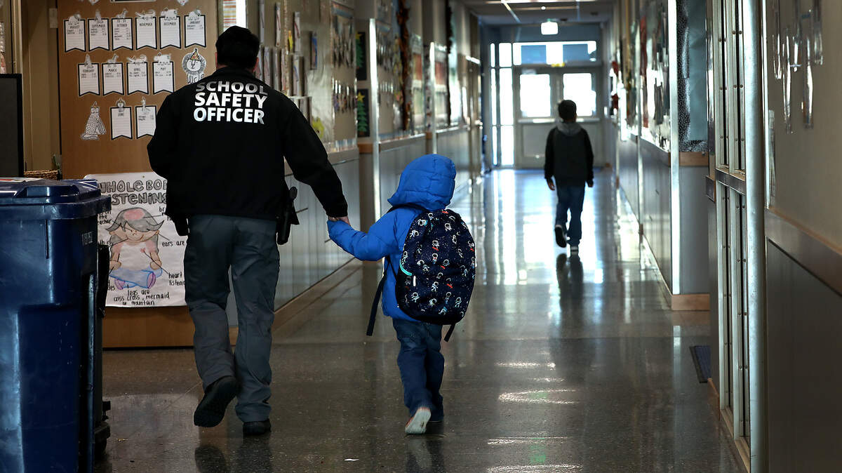 School safety officer Roman Trujillo walks a young late-arriving Amistad Elementary School student to his classroom recently in Kennewick. Trujillo is the most recent hire of the program that has reached full staffing in all the district's 17 elementary schools.