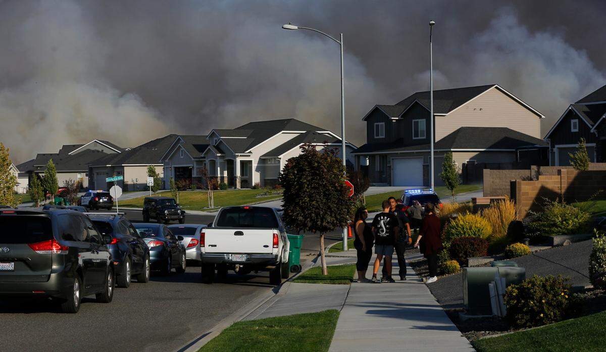 Heavy smoke darkens the sky behind homes on West 41st Avenue near Southridge Boulevard after a brush fire that started near I-82 spread to a commercial building and threatened houses in Kennewick.