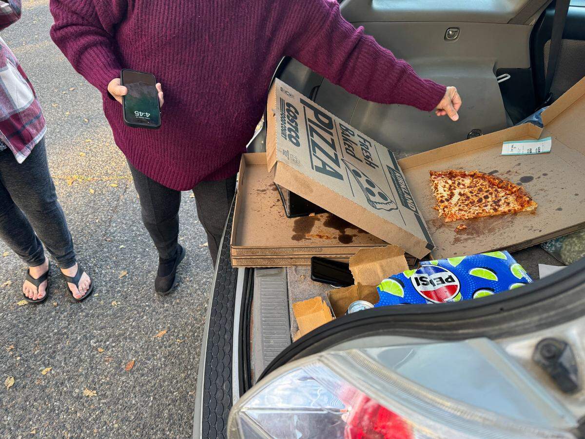 A volunteer working with the homeless community goes to close a pizza box after people served themselves Friday afternoon in Columbia Park.