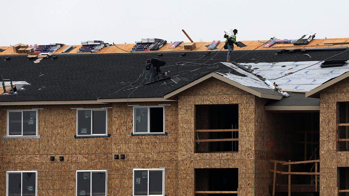 A pair of roofers work on top of a new building.