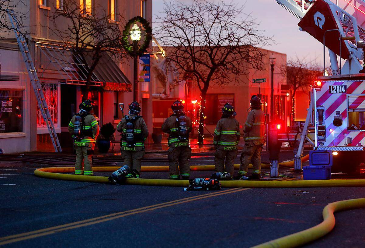 Firefighters stand ready during Friday’s early morning blaze the destroyed apartments and damaged shops of an historic downtown Kennewick building on the corner of Cascade Street and Kennewick Avenue. Fire department leaders kept the crews out of the building for safety reasons.