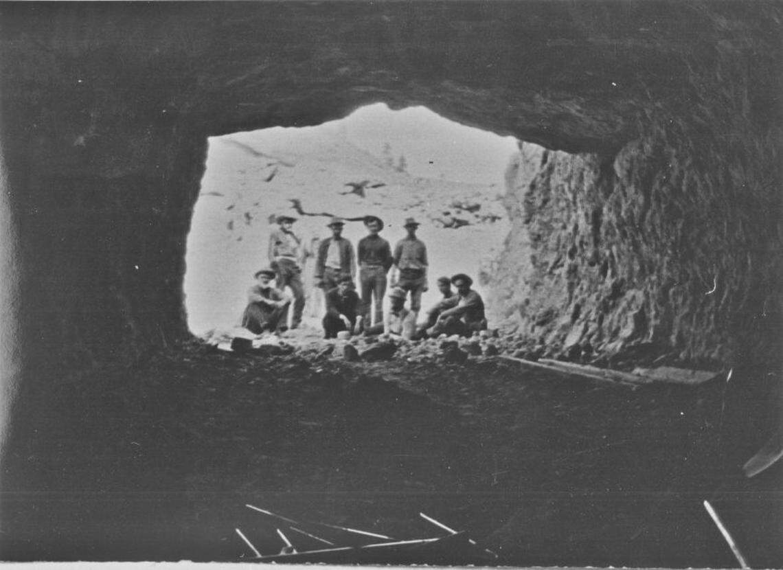 Group of ten people at mine portal looking in; view is looking out of mine at Ruby Mine near Nighthawk. Dr. Ecki with white beard on left.