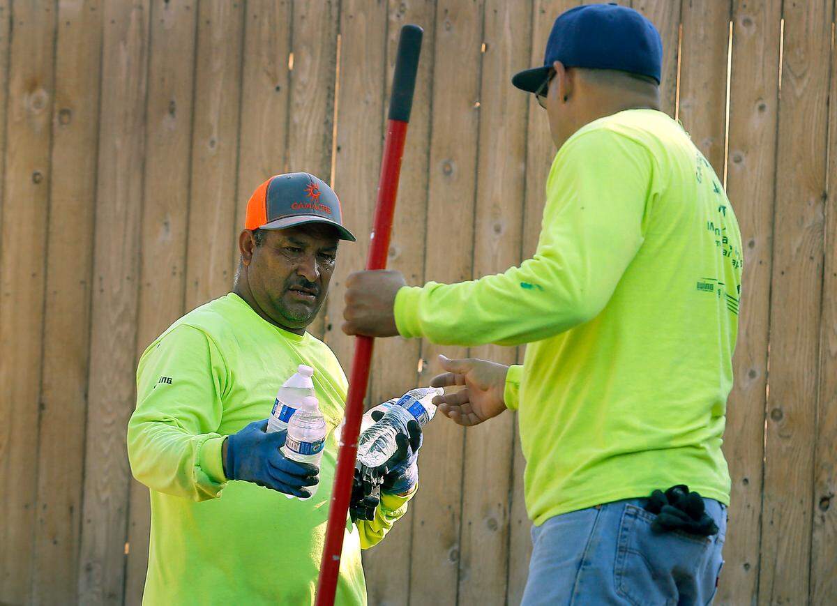 A landscaping worker shares bottles of water during a 2022 heat wave. Washington labor law requires employers to protect workers and provide cool water when temperatures rise.