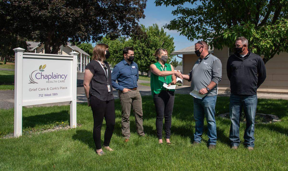 Jarrod Bailey, manager of Tri-Cities RDO Equipment, second from right, shakes hands with Brandy Hickey, manager of Cork’s Place, after handing her a check for $20,000 to expand the center’s programs helping grieving teens share their grief in a safe, supportive environment. RDO presented the checks for two Offutt Family Foundation grants to address youth suicide in the community during a ceremony outside of the Chaplaincy Cork’s Place Grief Support Center in Kennewick on Friday.