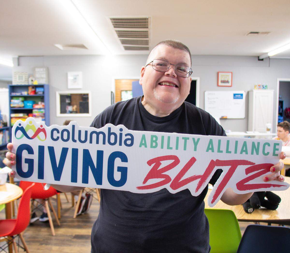 A Columbia Ability Alliance client, Kelly Morris, proudly holds up a sign while preparing for the 2025 Giving Blitz.